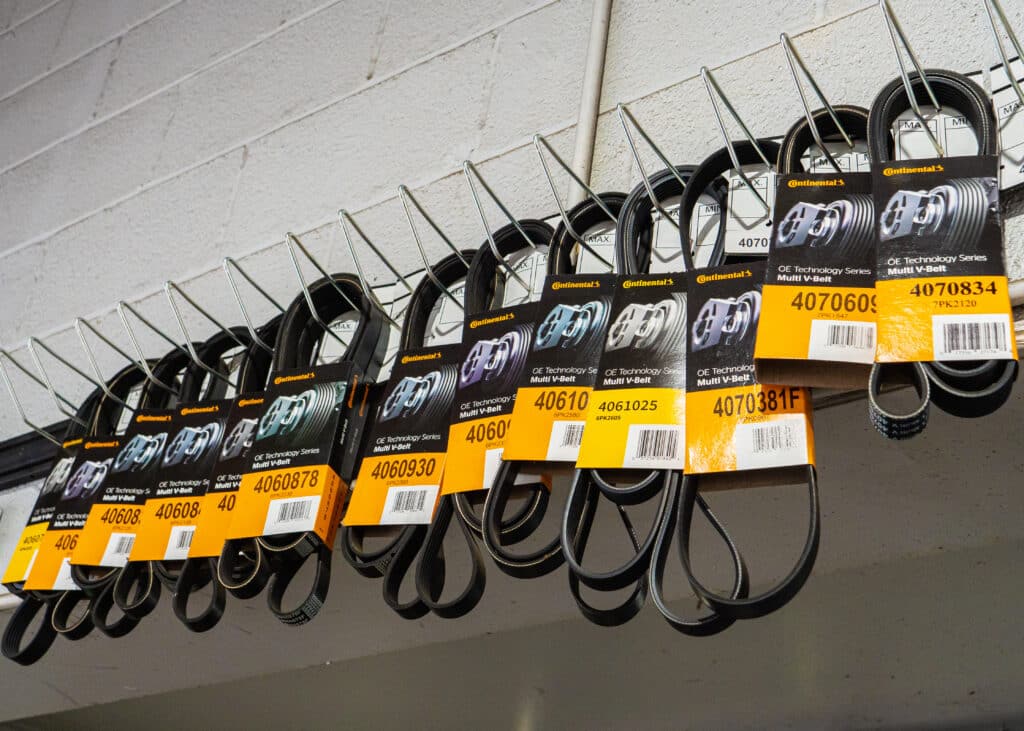 A row of engine belts hanging on hooks from the wall of the auto shop.